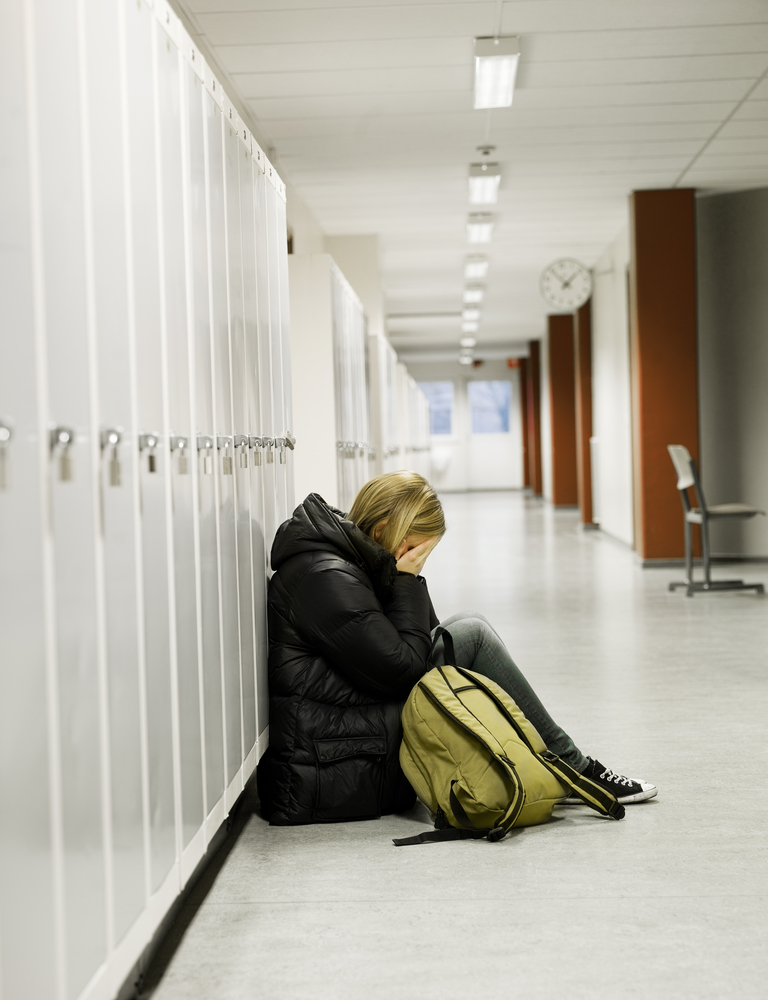 ragazza seduta a terra nel corridoio vuoto della scuola